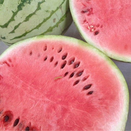 sliced watermelon with pink flesh and black seeds with one whole watermelon in light green with dark green stripes