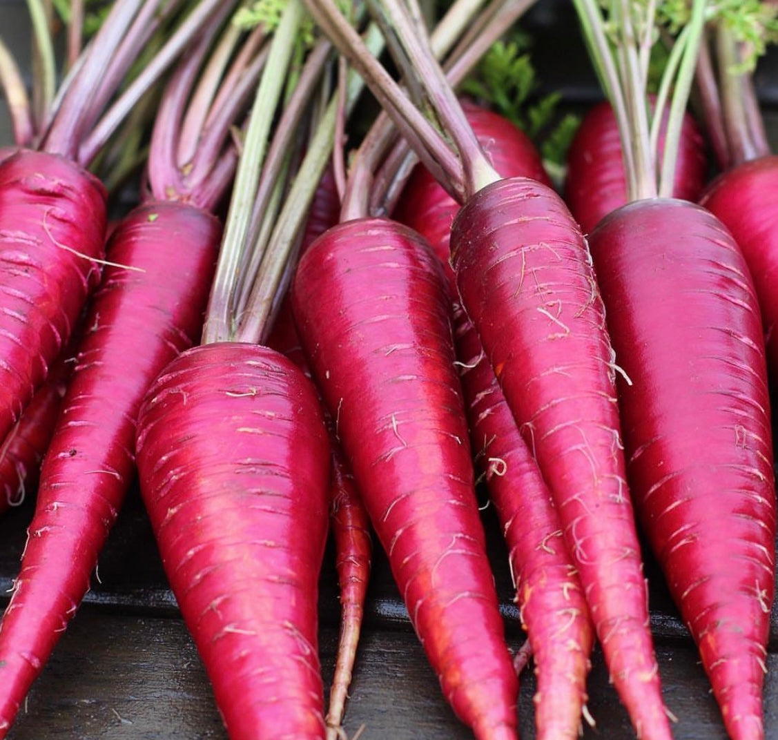 group of cosmic purple carrots with greens on a wooden table